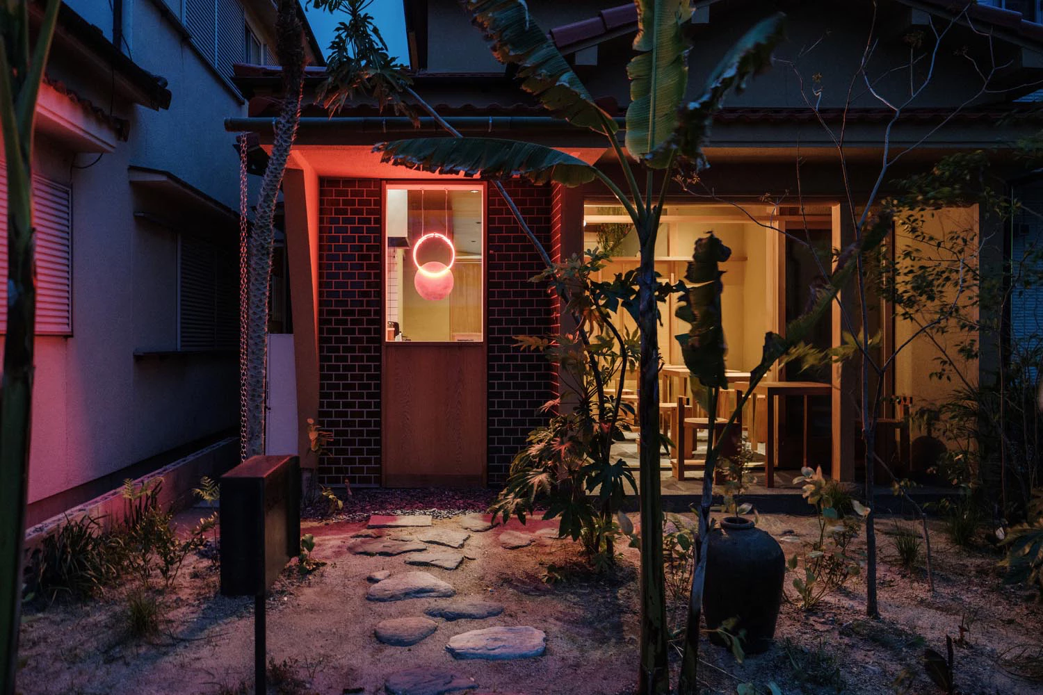 Japanese courtyard garden with neon-lit brick facade at night