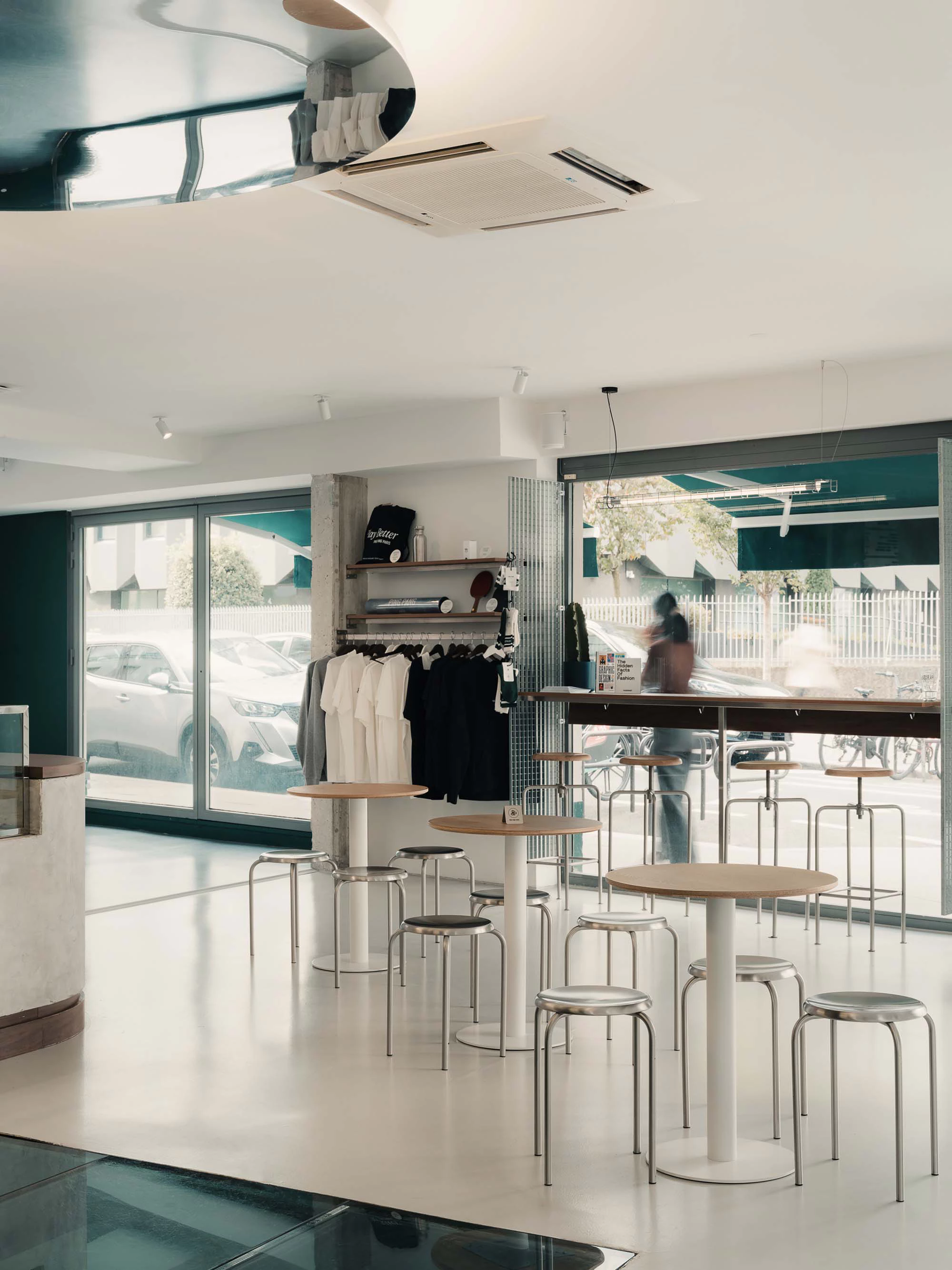 Bright cafe-boutique hybrid with round tables and clothing rack